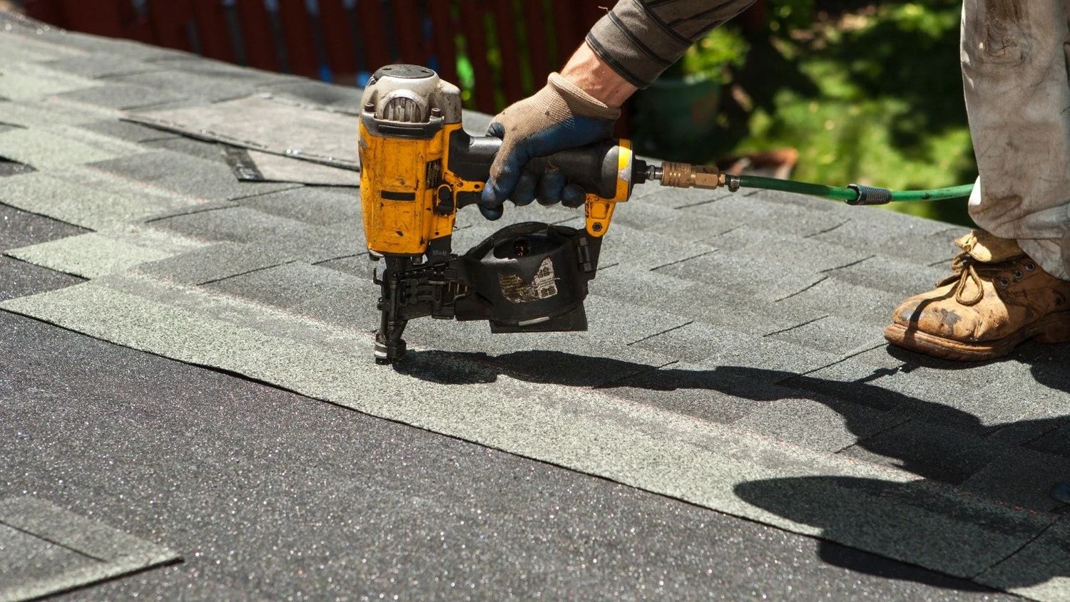 Roofing professional using a pneumatic nail gun to install asphalt shingles