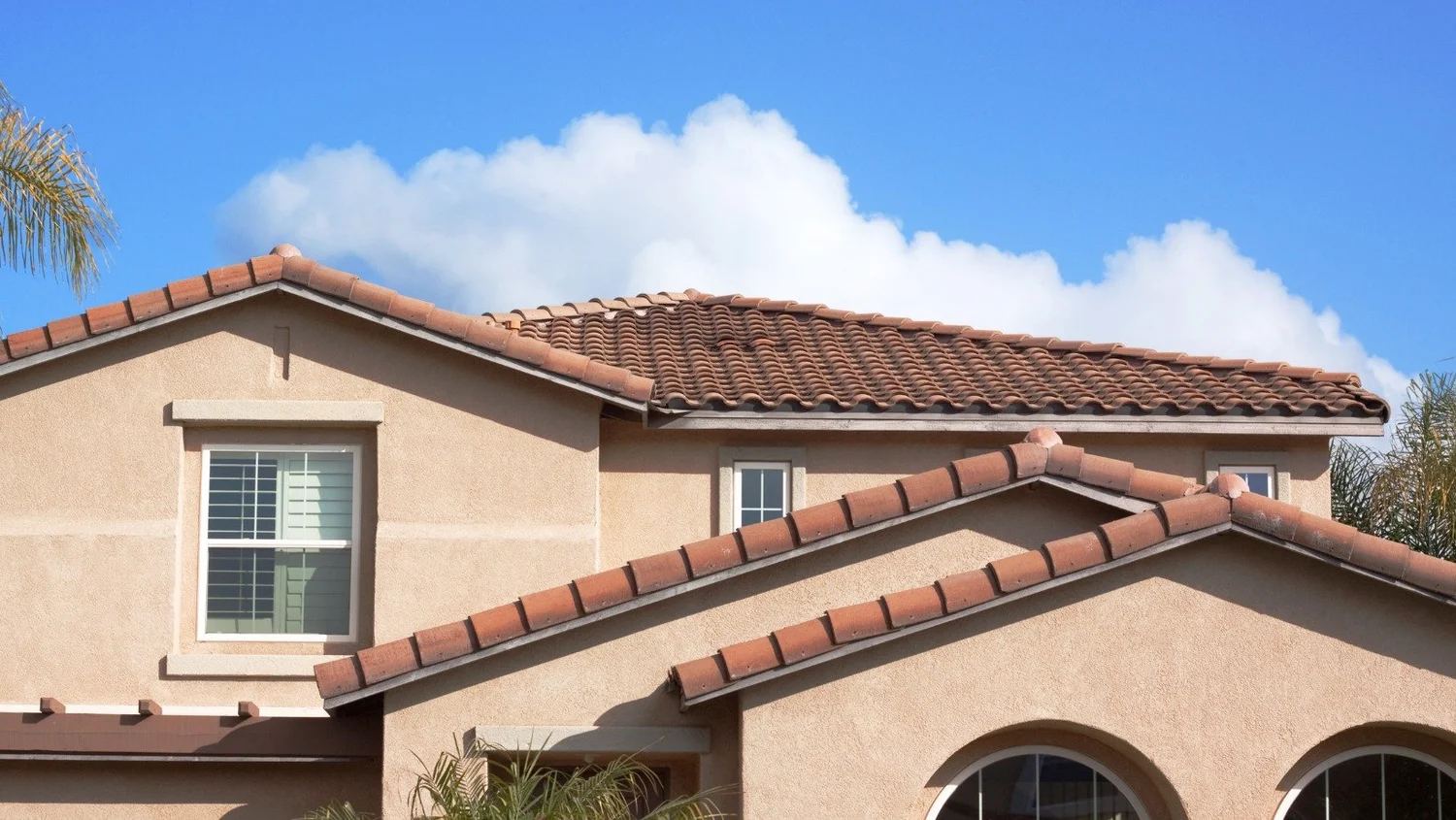 Mediterranean-style stucco home with terracotta clay tile roof against a blue Florida sky